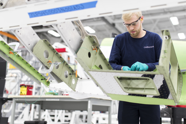 A technician working on an aircraft wing assembly in a manufacturing facility
