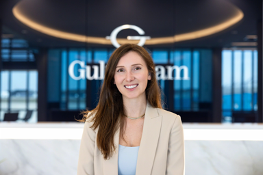 A woman in a light blazer stands in front of a Gulfstream logo