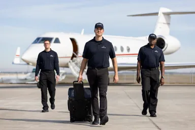Three uniformed personnel walking towards a private jet on an airport tarmac